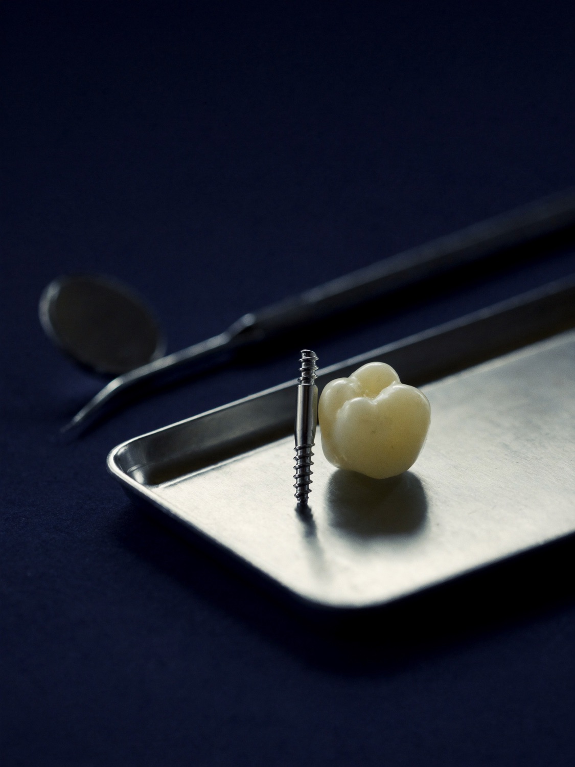 Titan-Implantat und Keramikkrone auf einem Instrumententablett